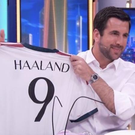 Enrique Riquelme segurando camisa do Real Madrid com nome de Haaland